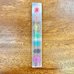 Vividly colored chakra symbols engraved on a Selenite Chakra Token on a wooden surface.