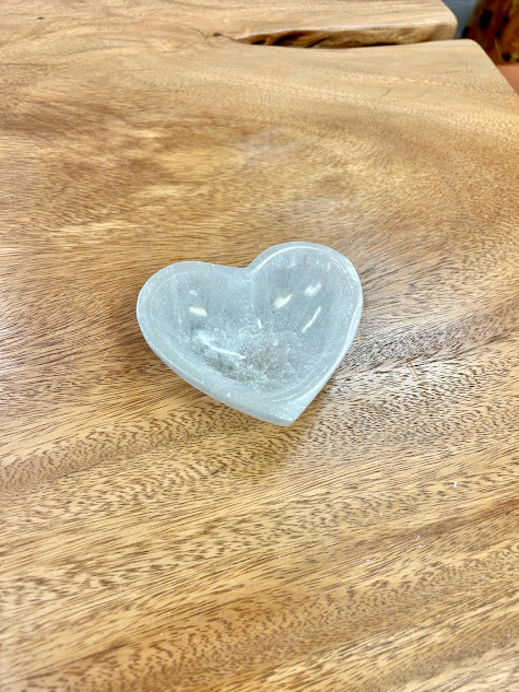 Angled view of the Selenite Heart Bowl on a wood background, showing off its polished surface and soft contours.