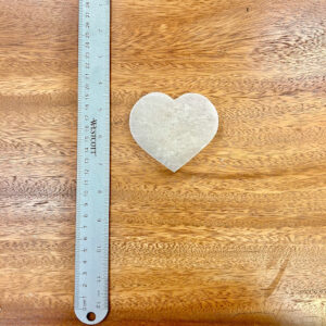 Heart-shaped selenite crystal piece on wood grain background symbolizing love and clarity.