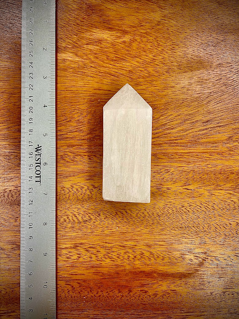 Selenite Obelisk next to a ruler on a wooden surface, demonstrating its height and elegant form.