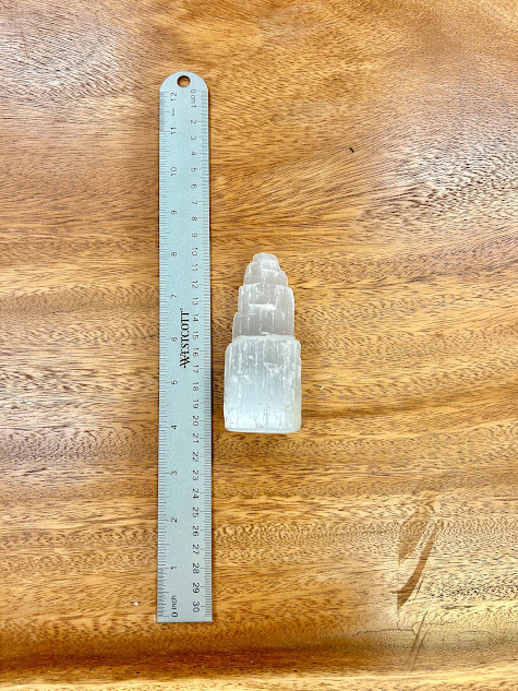 Selenite Small Tower alongside a ruler on a wooden surface, depicting its size.