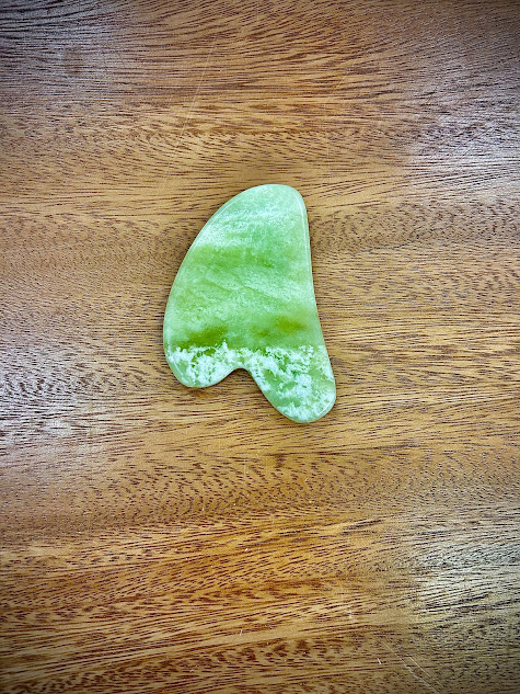 Jade Gua Sha tool on wooden surface highlighting its smooth, sculpting shape.